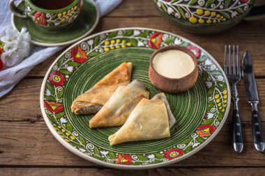 Dolgu ve sos ile haddelenmiş krep rustik ahşap masada çiçek desenli plaka üzerinde hizmet