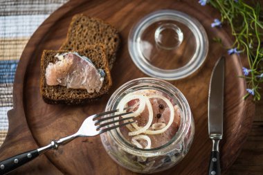 Soğan ekmek dilimleri ile ahşap tepsi üzerinde cam kavanoza salamura balık