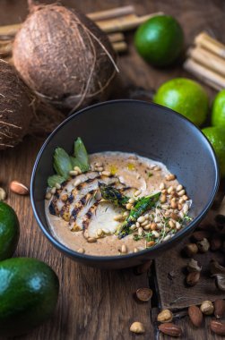 Tay çorba, et, fındık ve sebze malzemelerle ahşap masa üzerinde siyah kase krem