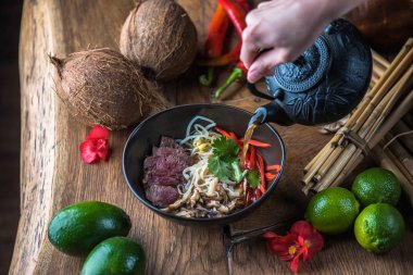 insan el Vietnamca Pho su dökerek ahşap masa üzerinde siyah kase çorba