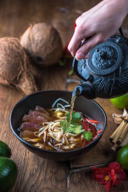 insan el Vietnamca Pho su dökerek ahşap masa üzerinde siyah kase çorba