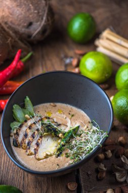 Tay çorba, et, fındık ve sebze malzemelerle ahşap masa üzerinde siyah kase krem
