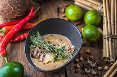 Tay çorba, et, fındık ve sebze malzemelerle ahşap masa üzerinde siyah kase krem