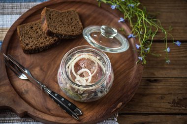 Soğan ekmek dilimleri ile ahşap tepsi üzerinde cam kavanoza salamura balık
