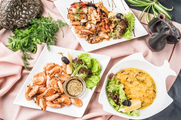 Different seafood dishes served on pink tablecloth with decor and herbs