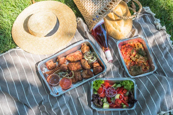 grilled meat, salad and vegetables in take away containers on blanket outdoors