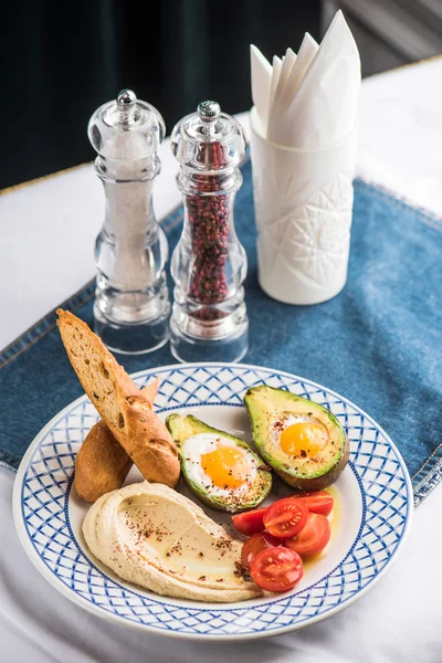 Avokado, domates, ekmek ve tabak üzerinde kızarmış yumurta ile ev yapımı humus