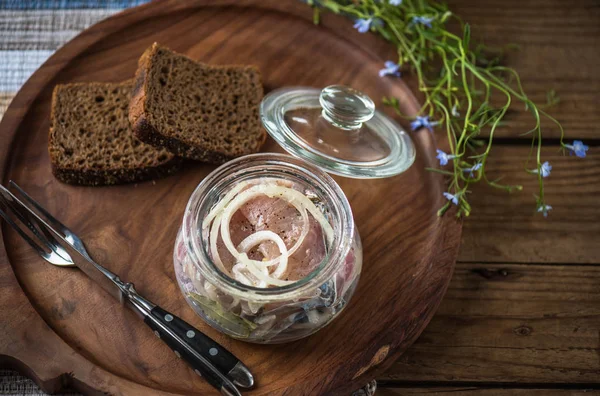 Soğan ekmek dilimleri ile ahşap tepsi üzerinde cam kavanoza salamura balık