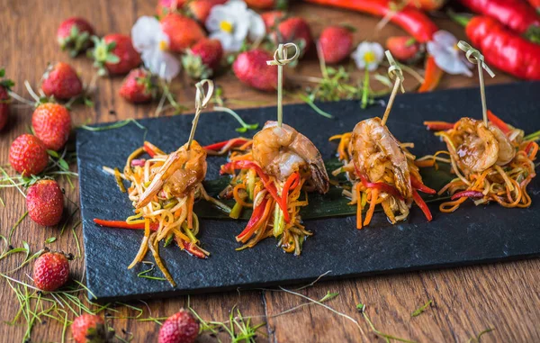 Seafood snack with vegetables on skewers served on slate