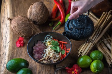 insan el Vietnamca Pho su dökerek ahşap masa üzerinde siyah kase çorba