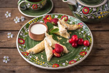 Taze çilek ve ekşi krem ile çiçek desenli plaka üzerinde tatlı haddelenmiş krep