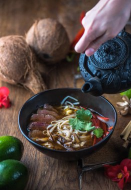 insan el Vietnamca Pho su dökerek ahşap masa üzerinde siyah kase çorba