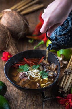 insan el Vietnamca Pho su dökerek ahşap masa üzerinde siyah kase çorba