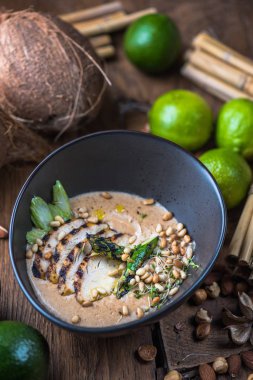 Tay çorba, et, fındık ve sebze malzemelerle ahşap masa üzerinde siyah kase krem