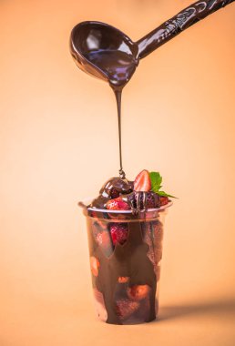 bej renkli arka plan üzerinde eritilmiş çikolata ile plastik kap içinde dökme taze çilek