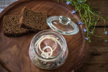 Soğan ekmek dilimleri ile ahşap tepsi üzerinde cam kavanoza salamura balık