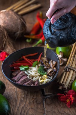 insan el Vietnamca Pho su dökerek ahşap masa üzerinde siyah kase çorba