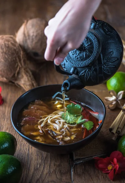 insan el Vietnamca Pho su dökerek ahşap masa üzerinde siyah kase çorba