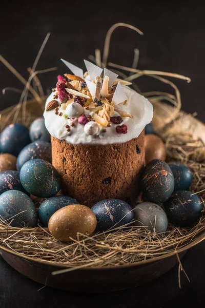 Şekerlenmiş meyve ile lezzetli tatlı Paskalya kek, çikolata ve boyalı yumurtalar sepette koyu arka plan üzerinde