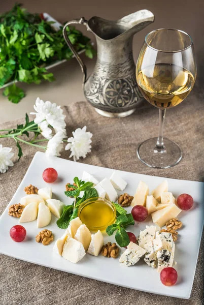 Beyaz şarap bir bardak gri masa örtüsü üzerinde peynir tabağı