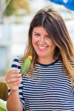 çiftçi pazarında küçük salatalık tutan gülümseyen genç kadın
