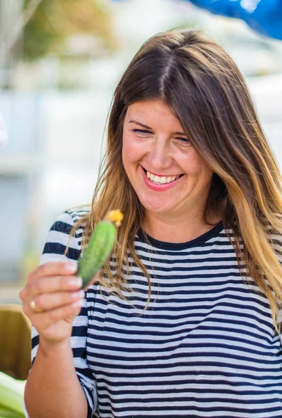 çiftçi pazarında küçük salatalık tutan gülümseyen genç kadın