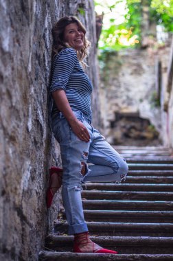 şehirde eski merdivenlerde duvara eğilme gülümseyen genç kadın