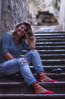 şehirde eski merdivenlerde oturan gülümseyen genç kadın