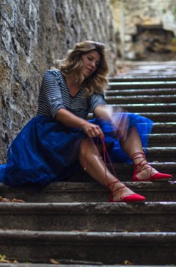 Eski merdivenlerde oturan ve şehirde Ayakkabı bağlama gülümseyen genç kadın