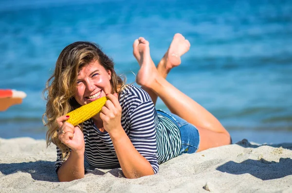 Положительная Женщина Лежит Песчаном Пляже Ест Кукурузный Початок — стоковое фото