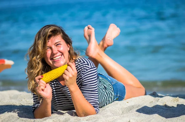Положительная Женщина Лежит Песчаном Пляже Ест Кукурузный Початок — стоковое фото