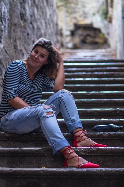 şehirde eski merdivenlerde oturan gülümseyen genç kadın