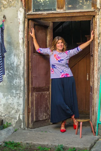 Positive woman standing in door frame of shabby rustic house in countryside