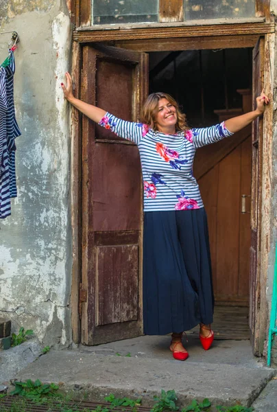 Positive woman standing in door frame of shabby rustic house in countryside