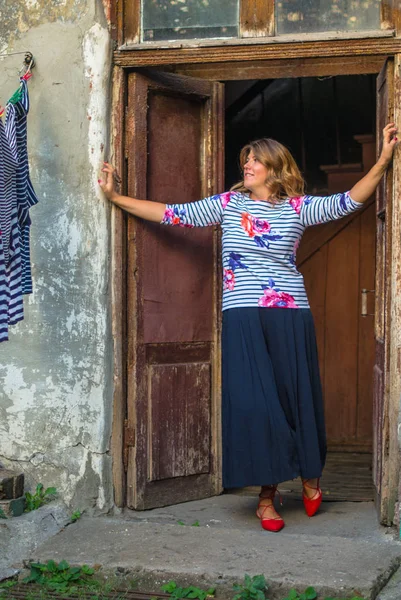 Positive woman standing in door frame of shabby rustic house in countryside