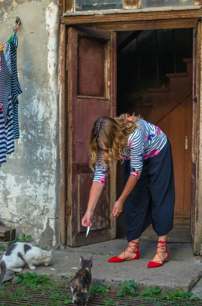 woman feeding cat with anchovy in bowl outdoors in countryside