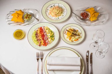 Birçok farklı yemek restoran tablo. Tabak, çatal, bıçak, beyaz masa örtüsü gözlük. Üstten Görünüm