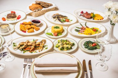 Birçok farklı yemek restoran tablo. Tabak, çatal, bıçak, beyaz masa örtüsü gözlük. Vazoda Çiçekler