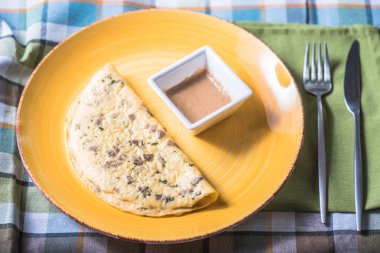 Damalı masa örtüsü üzerinde soslu tabakta otlar ile ev yapımı omlet