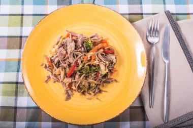 Tavuk ve sebze damalı masa örtüsü üzerinde sarı plaka ile Asya erişte