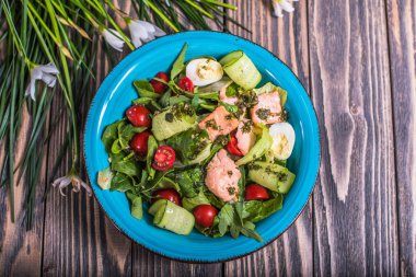 Taze sebze salatası somon ve çiçekler ile ahşap masa üzerinde bir kapta yumurta