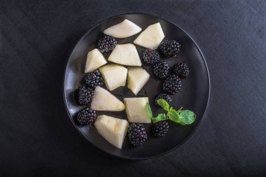 Siyah arka plan üzerinde taze böğürtlen ve kavun parçaları Tabak