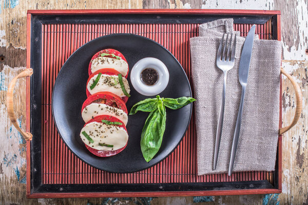 Tomatoes with cheese and basil on plate with sauce on wooden table