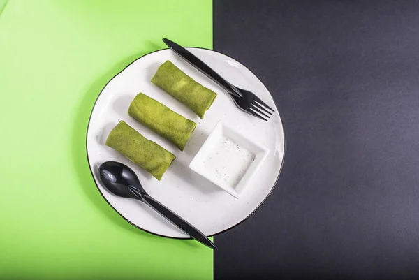 Vegetable green pancakes with dip on white plate on green and grey surface