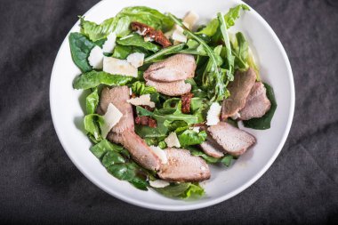 karanlık masa örtüsü üzerinde kase etli sebze salatası