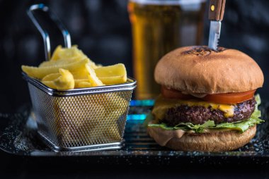 Sığır eti burger tepside koyu arka plan üzerinde kızarmış patates dilimleri ile servis