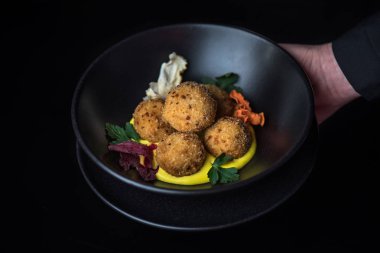 karanlık arka planda sos ile kızarmış mozzarella topları insan eli tutan kase