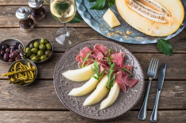 Aperatif plaka jambon ve kavun tabakta ahşap masa üzerinde beyaz şarap ile
