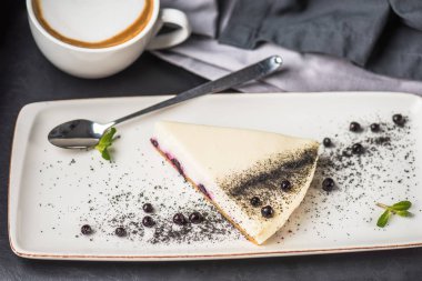 Berry cheesecake beyaz plaka üzerinde parça fincan kapuçino üzerinde gri masa örtüsü ile 