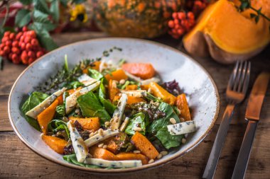 Sonbahar yaprakları ve meyveleri ile ahşap masa üzerinde peynirli taze sebze salatası